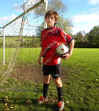 Young boy holding a soccer ball on a grassy field with a goalpost in the background.